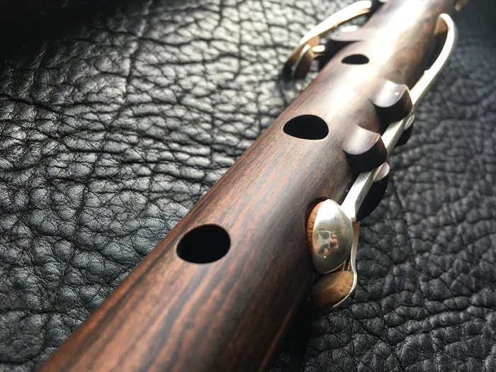 The body of a blackwood flute with silver keys and open tone holes, lying on black leather.