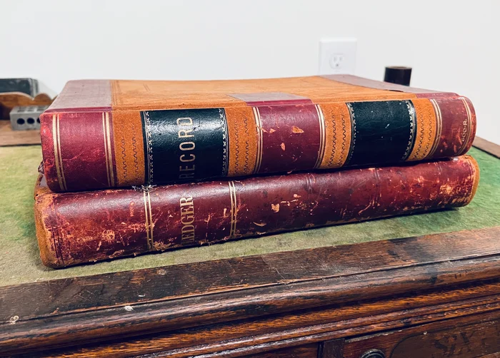 Two worn leather-bound ledgers stacked on a desk.