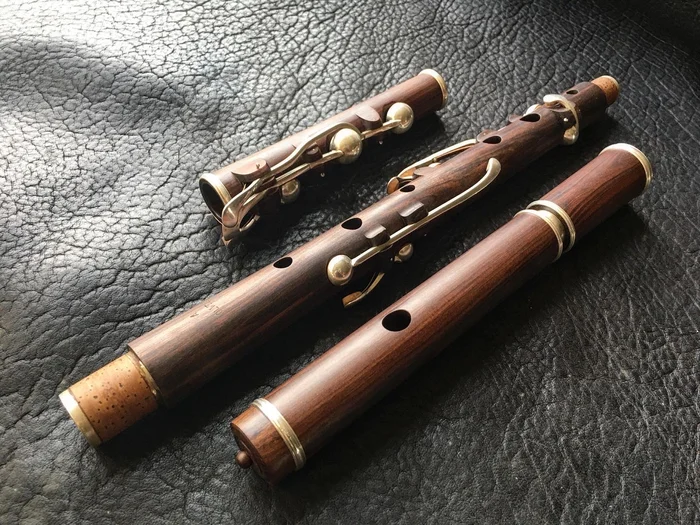 A keyed wooden flute taken apart into its sections, laid on black leather with brass ferrule rings showing.