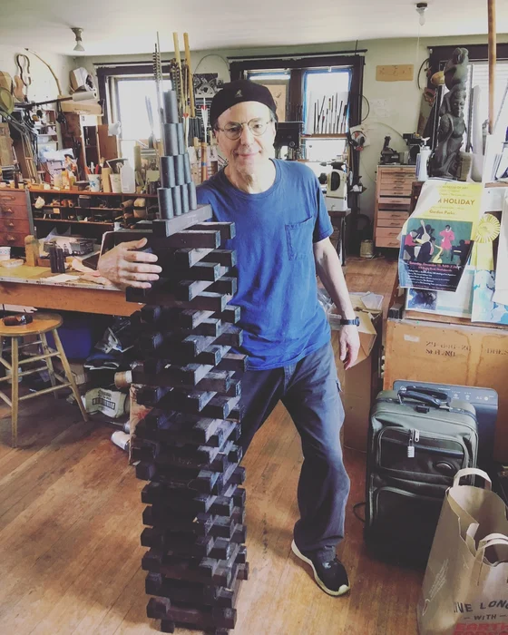 A maker in the workshop standing beside a tall stack of flute cases.